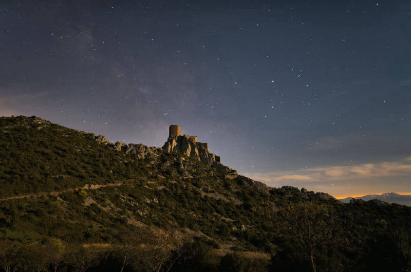Photographie nocturne (19 avril 2016 à 4 h 39) avec l’éclairage naturel de la lune (91 % ; photographie : Philippe Contal) - Le fin voile lumineux qui semble s'échapper de la silhouette de Quéribus est la Voie Lactée (9ᵉ place au concours Wiki Loves Monuments 2017 sur 245 000 images)